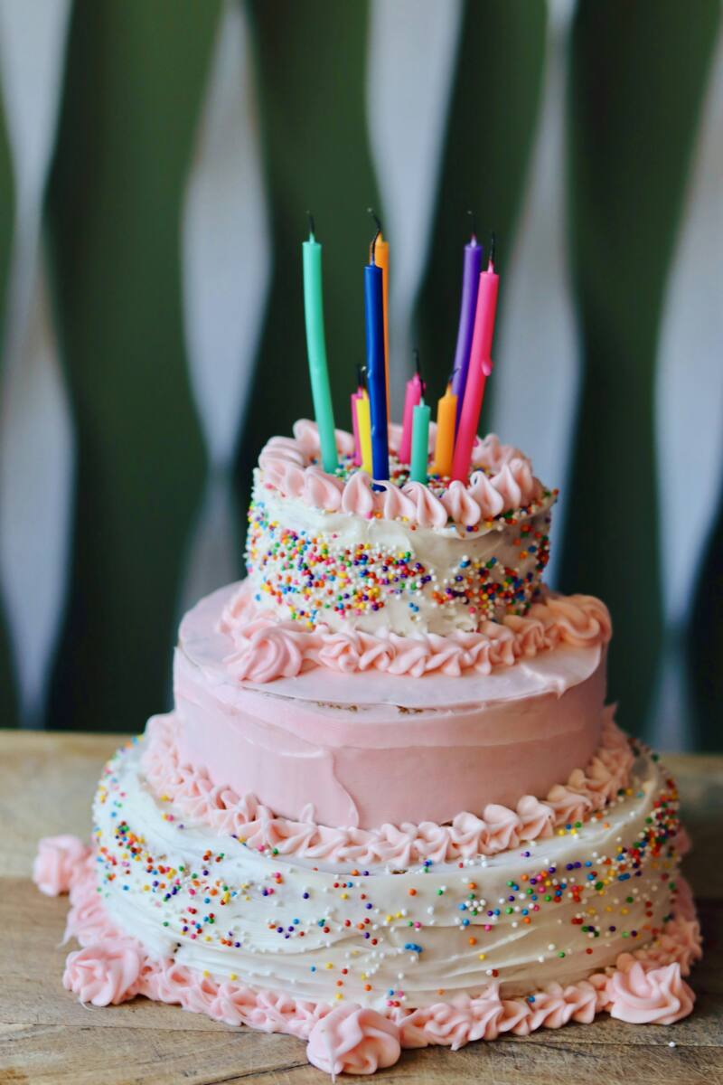 A pink three-tier birthday cake topped with colorful lit candles, one of many birthday phone case gift ideas to draw inspiration from