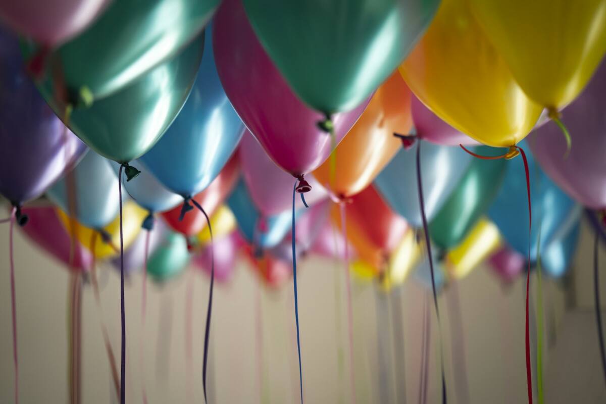 A cluster of colorful birthday balloons in teal, pink, orange, and yellow floating near a ceiling