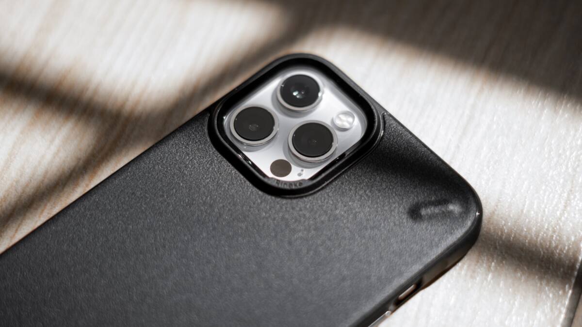 A black dark academia grunge phone case in moody, dramatic lighting on a wood surface