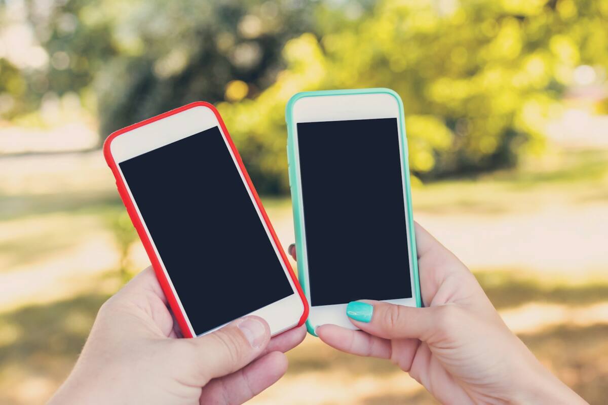 Two hands holding a his and hers matching phone case set in red and teal