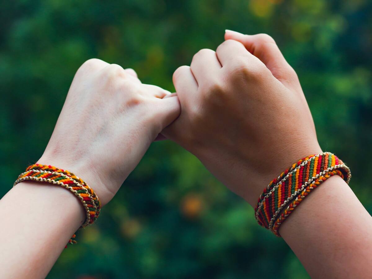 Two hands with matching friendship bracelets doing a pinky promise