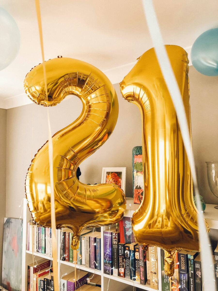 Large gold number 21 foil balloons hanging in a room with a bookshelf in the background