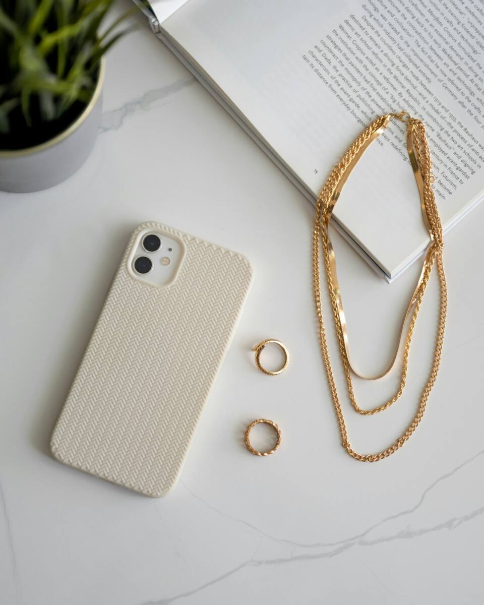 A cream minimalist cottagecore phone case styled with gold jewelry on a marble surface